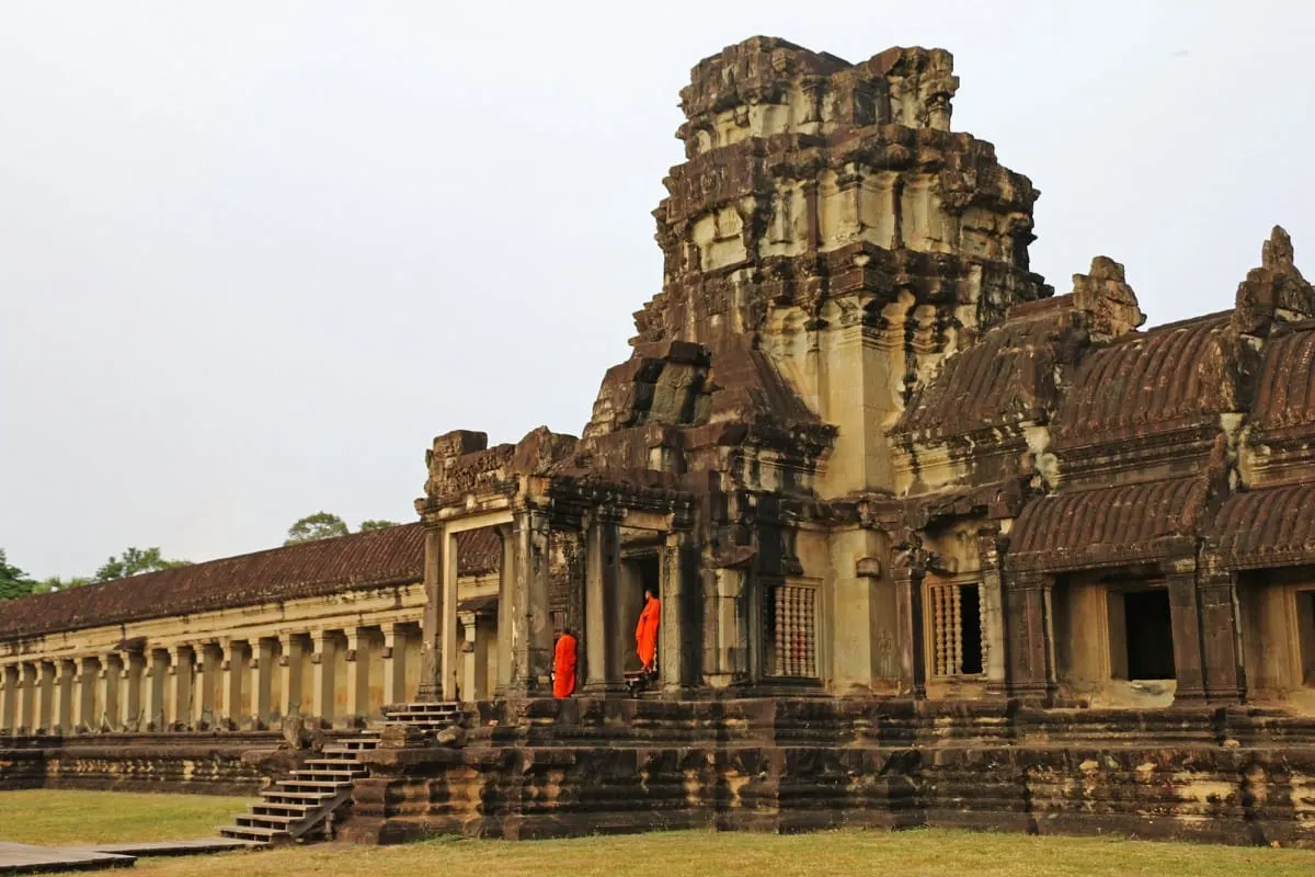 Two monks in orange robes at a gallery entrance of Angkor Wat.