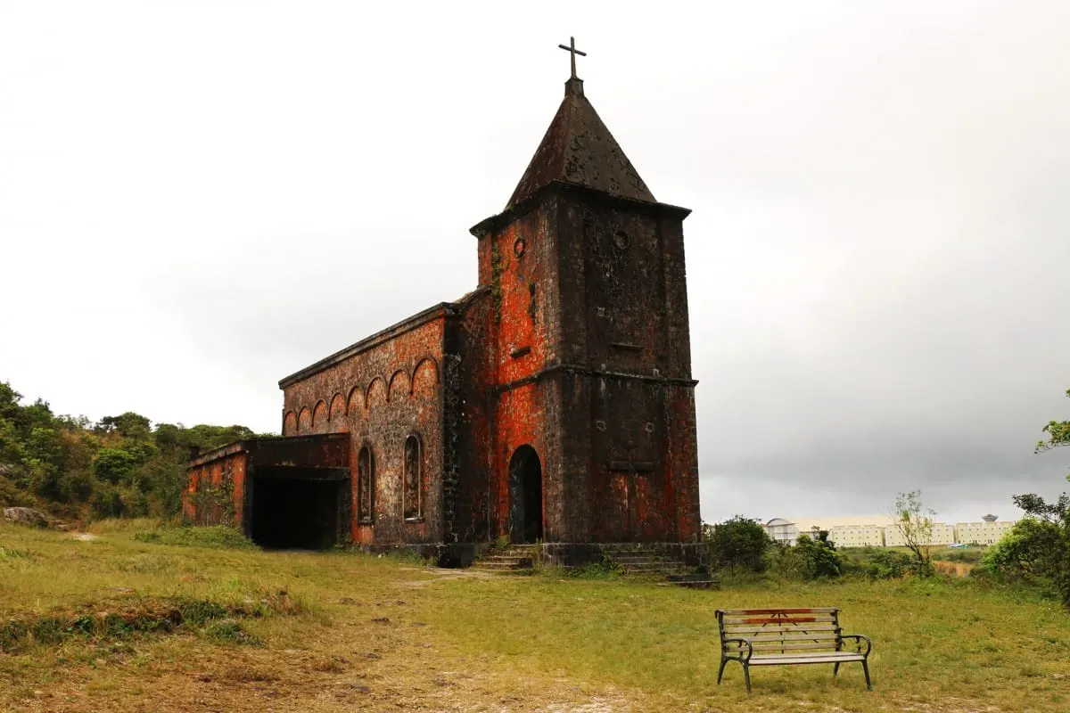 Old lichen-stained brick Catholic church with a bench in front, Bokor Hill Station.