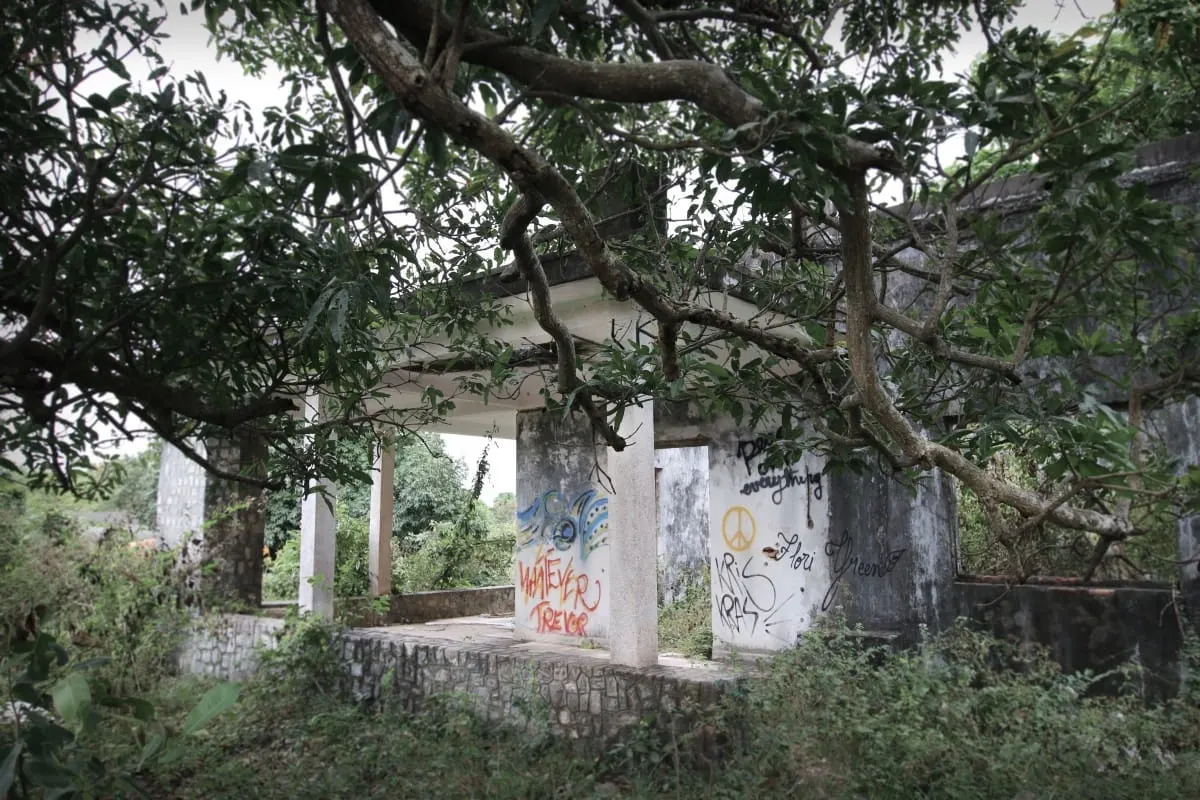 Graffiti-covered pillars of an abandoned villa beneath tree branches in Kep.
