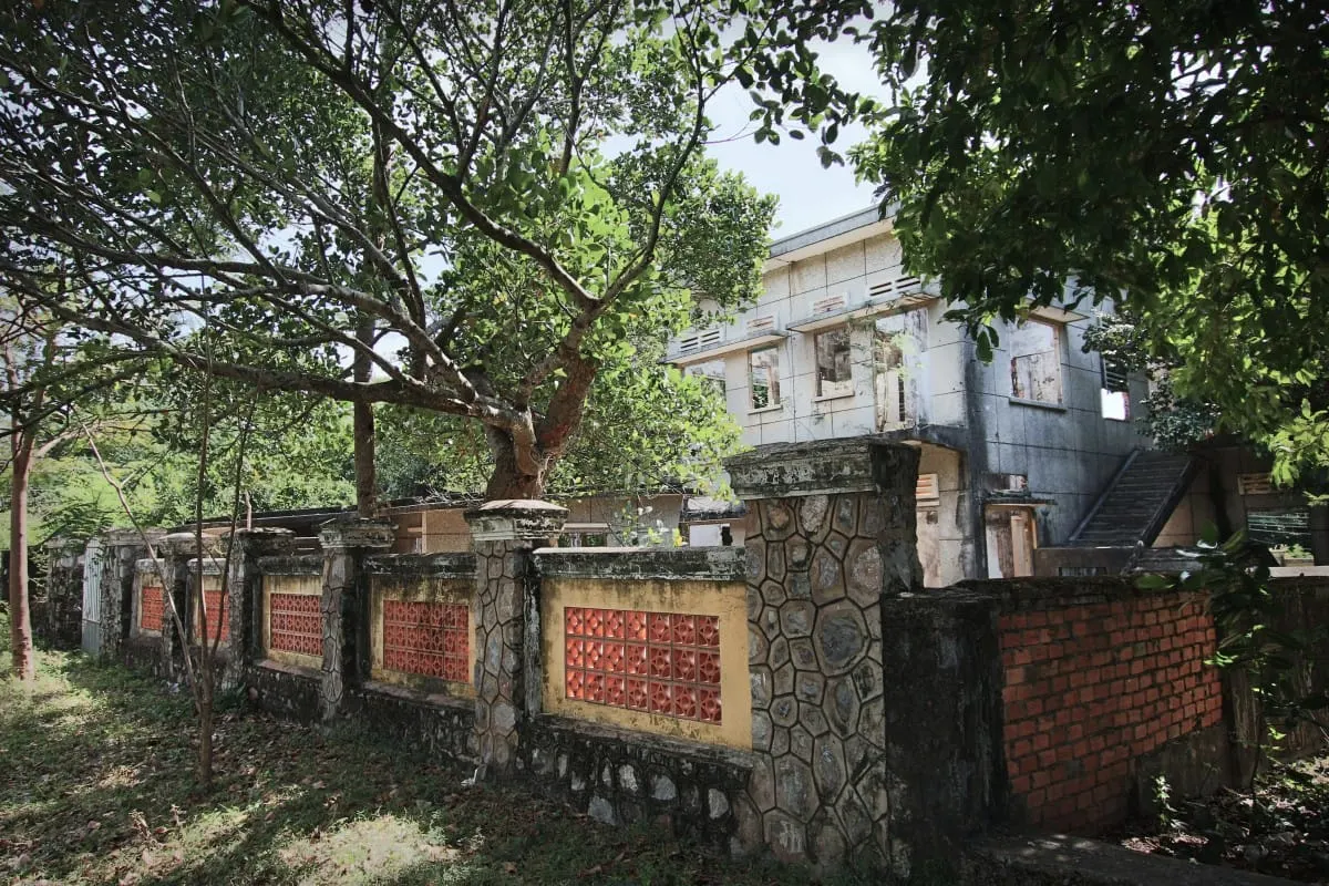 Stone garden wall with orange breeze blocks before an abandoned villa in Kep.