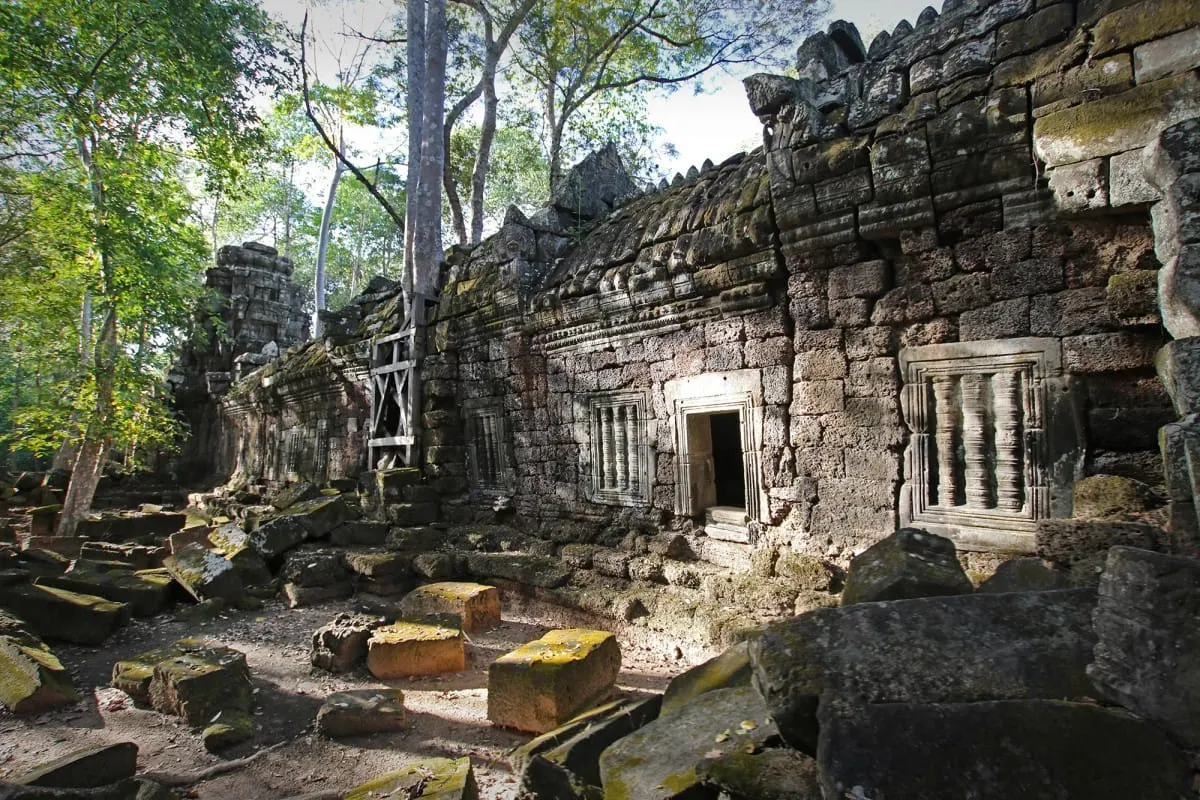 Moss-covered sandstone walls and fallen blocks of Ta Nei temple in the forest.