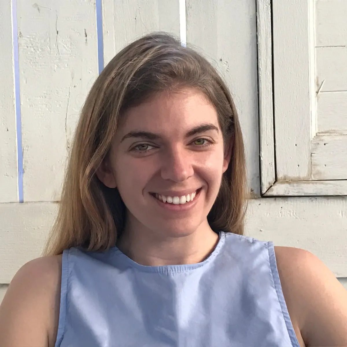 Smiling woman in a sleeveless blue top against a white wooden wall
