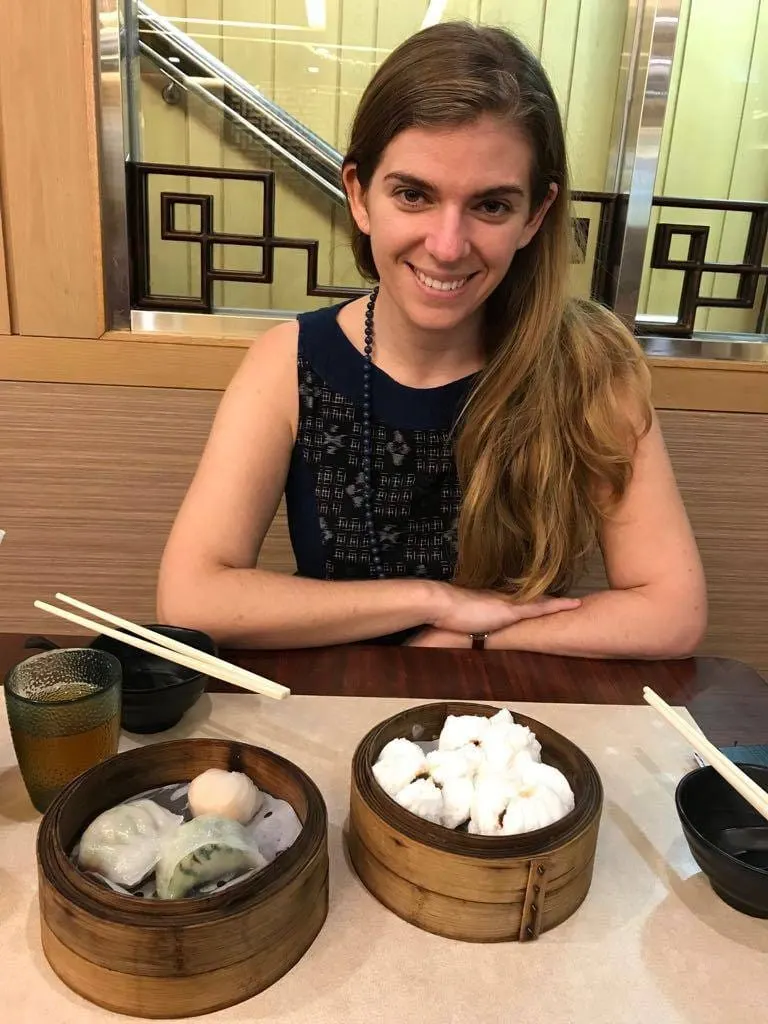 Smiling woman at a table with bamboo steamer baskets of dim sum in Hong Kong