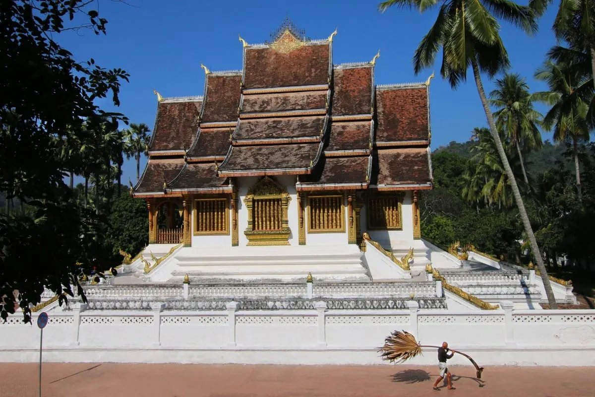 Haw Pha Bang temple's tiered roofs in Luang Prabang, a man carrying a palm frond past