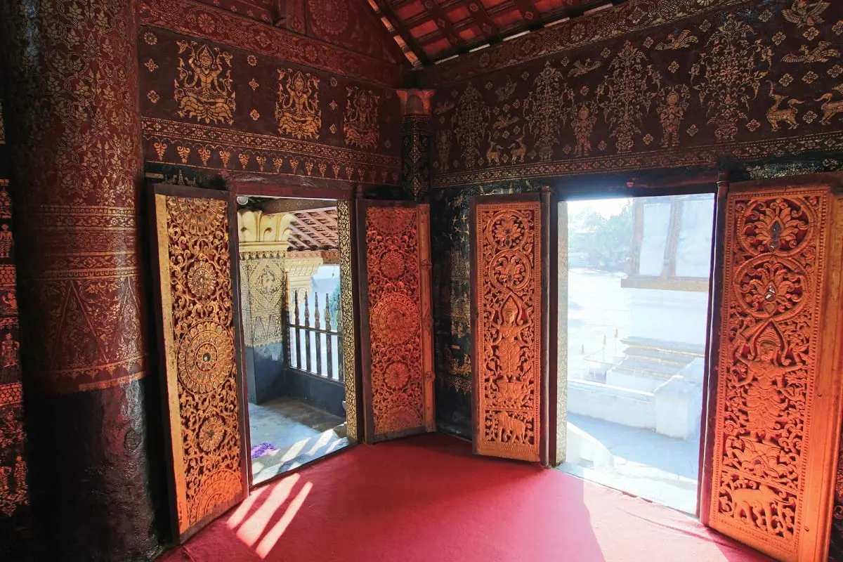 Open carved and gilded doors inside a red-lacquered temple hall, Luang Prabang
