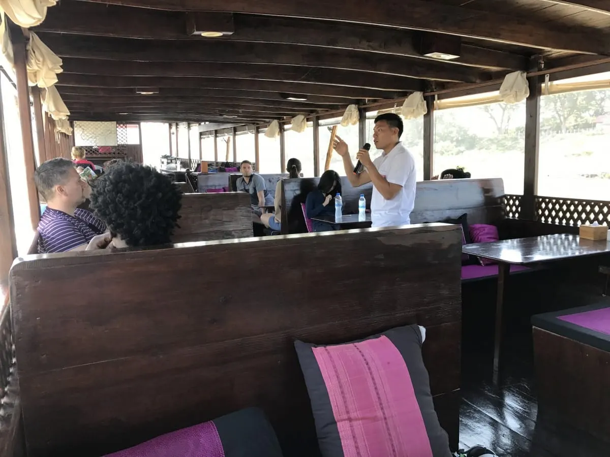 Guide with a microphone speaking to passengers aboard a Mekong slow boat