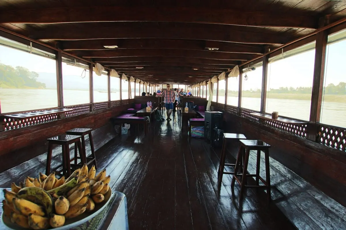 Wooden interior of a Mekong slow boat with stools and a plate of bananas