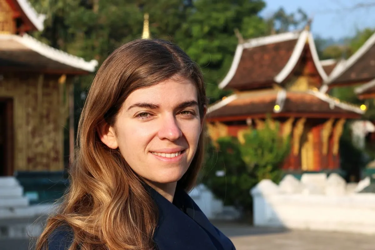 Smiling woman in morning light in front of Wat Xieng Thong temple buildings