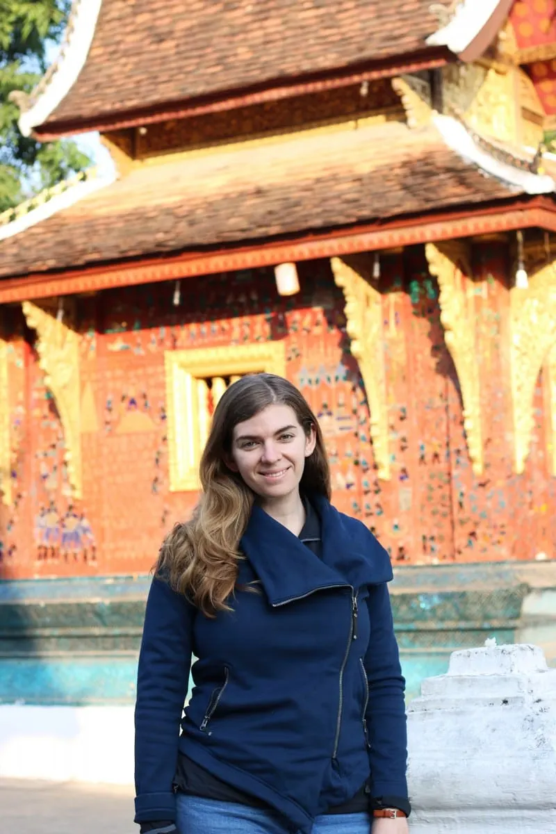 Woman posing before the red glass-mosaic wall of Wat Xieng Thong