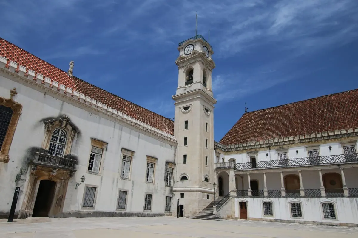 University of Coimbra clock tower between white buildings with red tile roofs