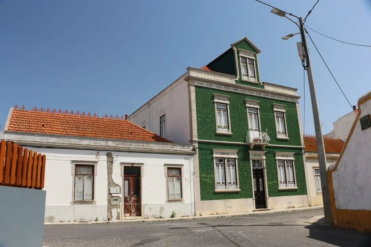 Green-tiled townhouse beside a white cottage on a quiet Peniche street