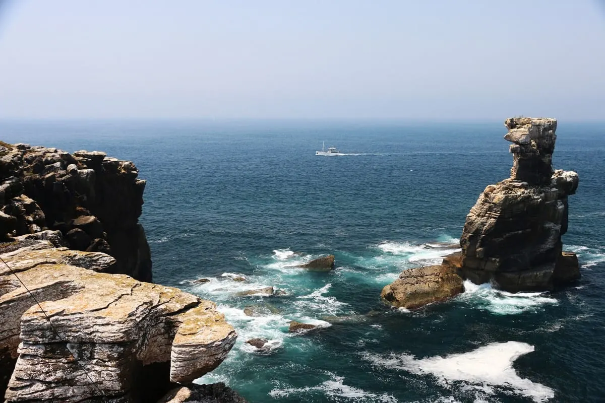 Rock sea stack off the Peniche coast with a boat on the Atlantic horizon