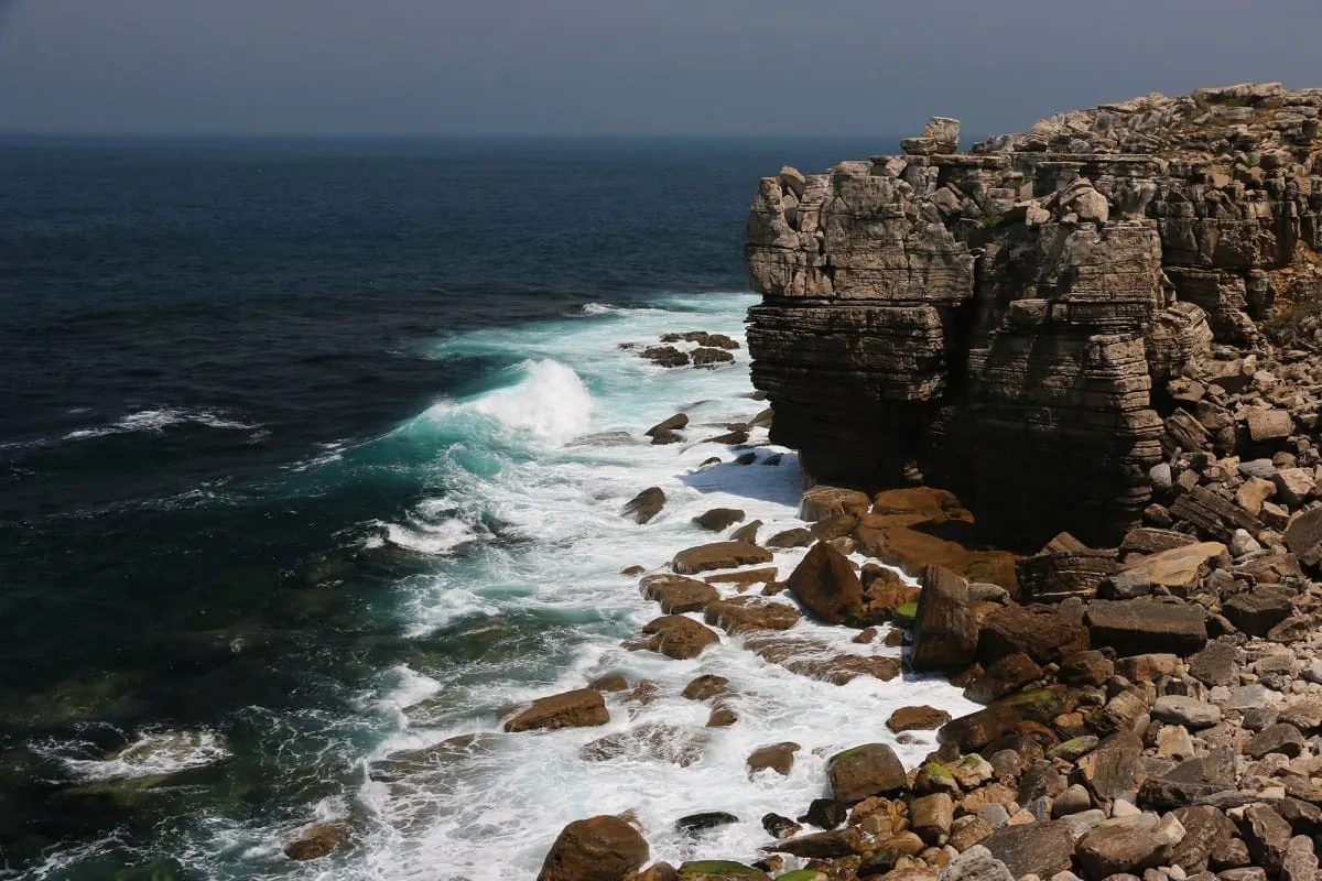 Layered limestone cliffs and boulders battered by Atlantic surf at Peniche