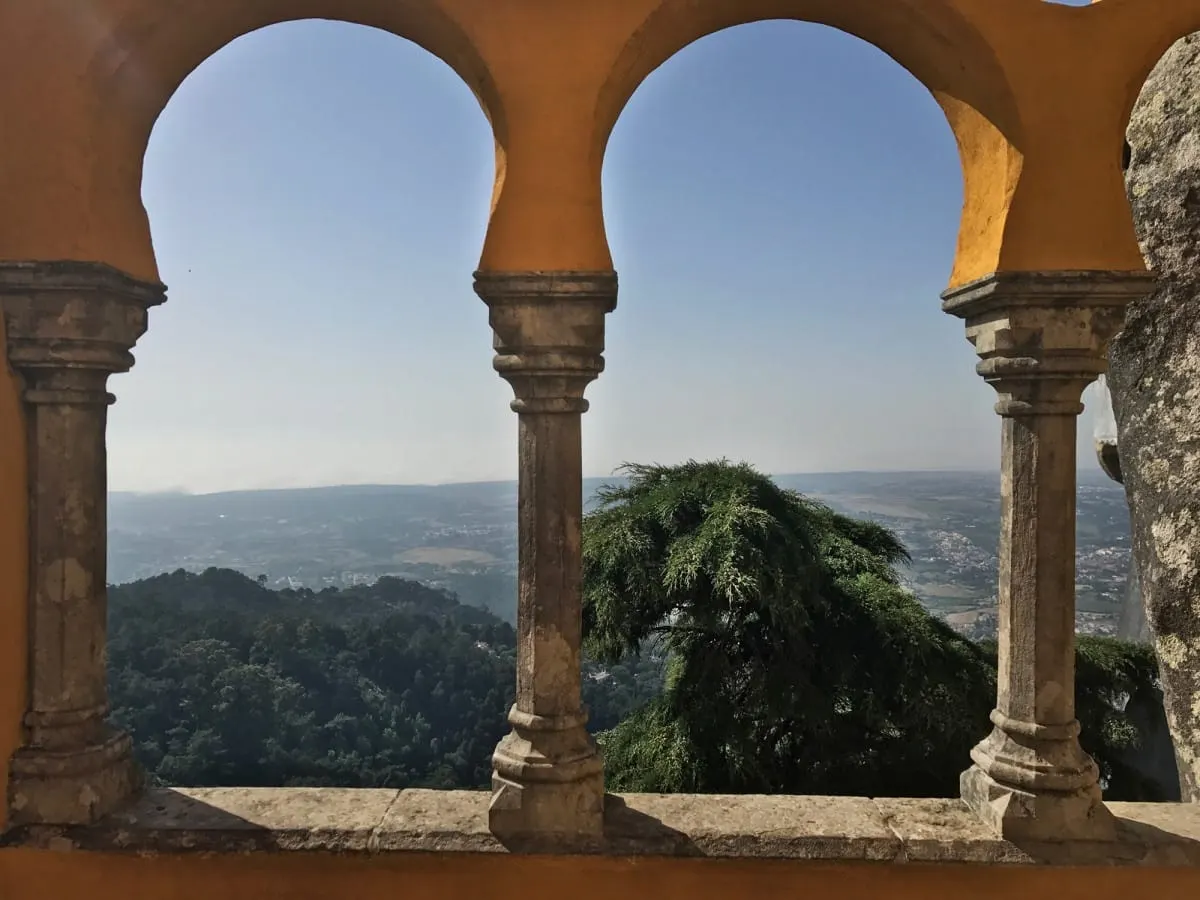Forested hills and plains seen through yellow arches at Pena Palace, Sintra