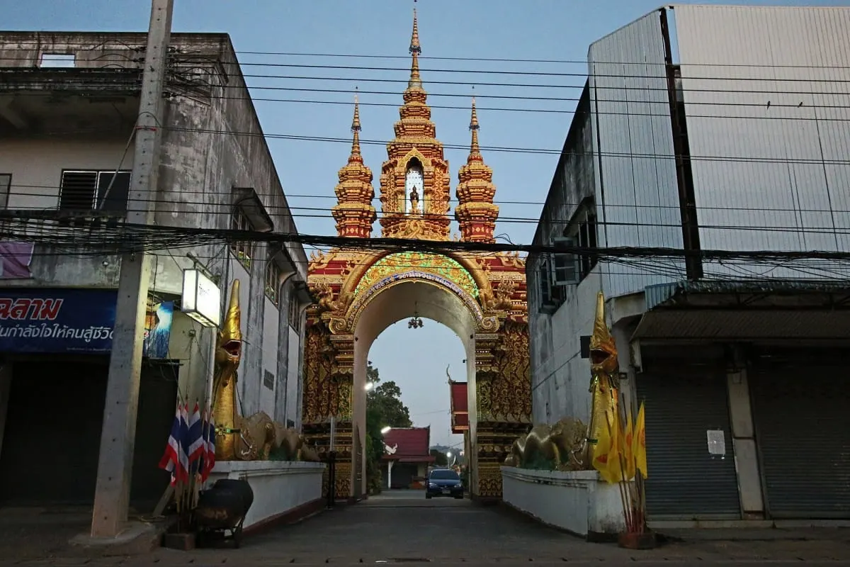 Gilded temple gateway with naga statues between shops in Chiang Khong