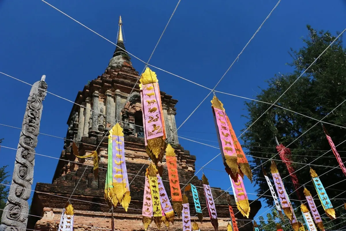 Colorful zodiac temple flags strung before an ancient brick chedi, Chiang Mai