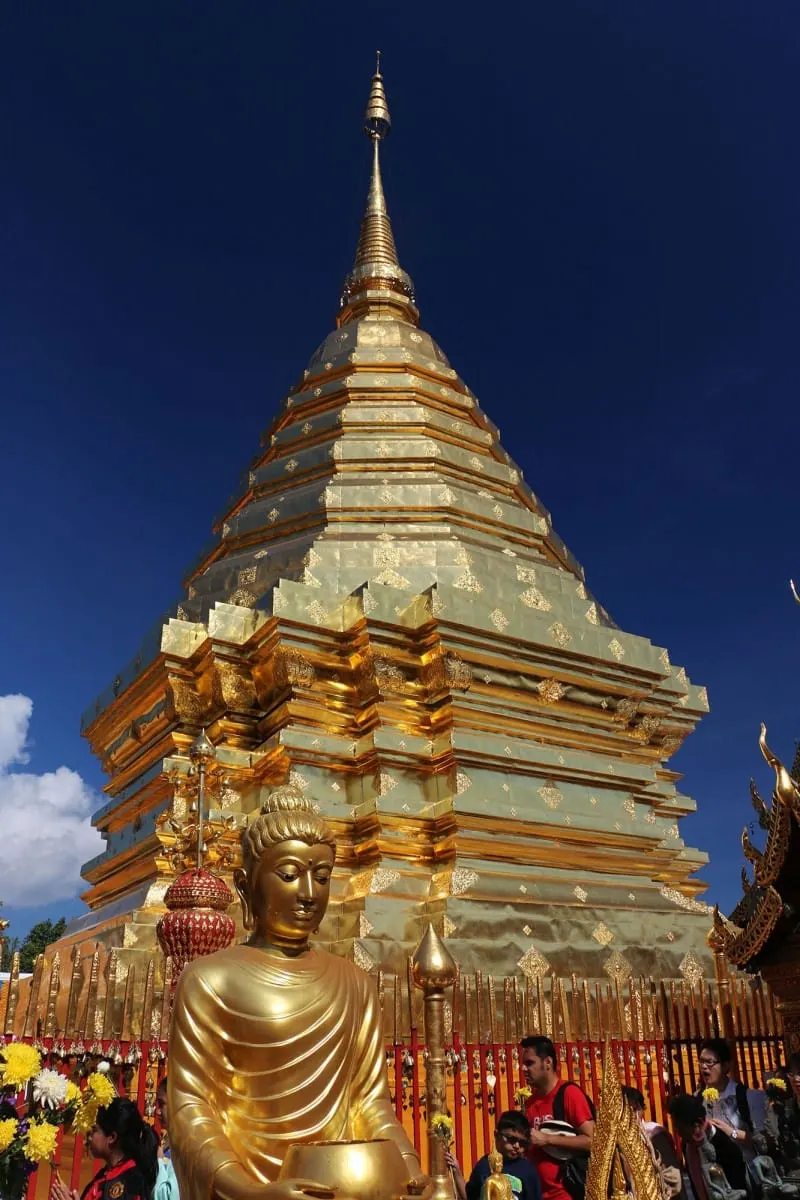 Golden Buddha statue before a gleaming gold chedi under a deep blue sky
