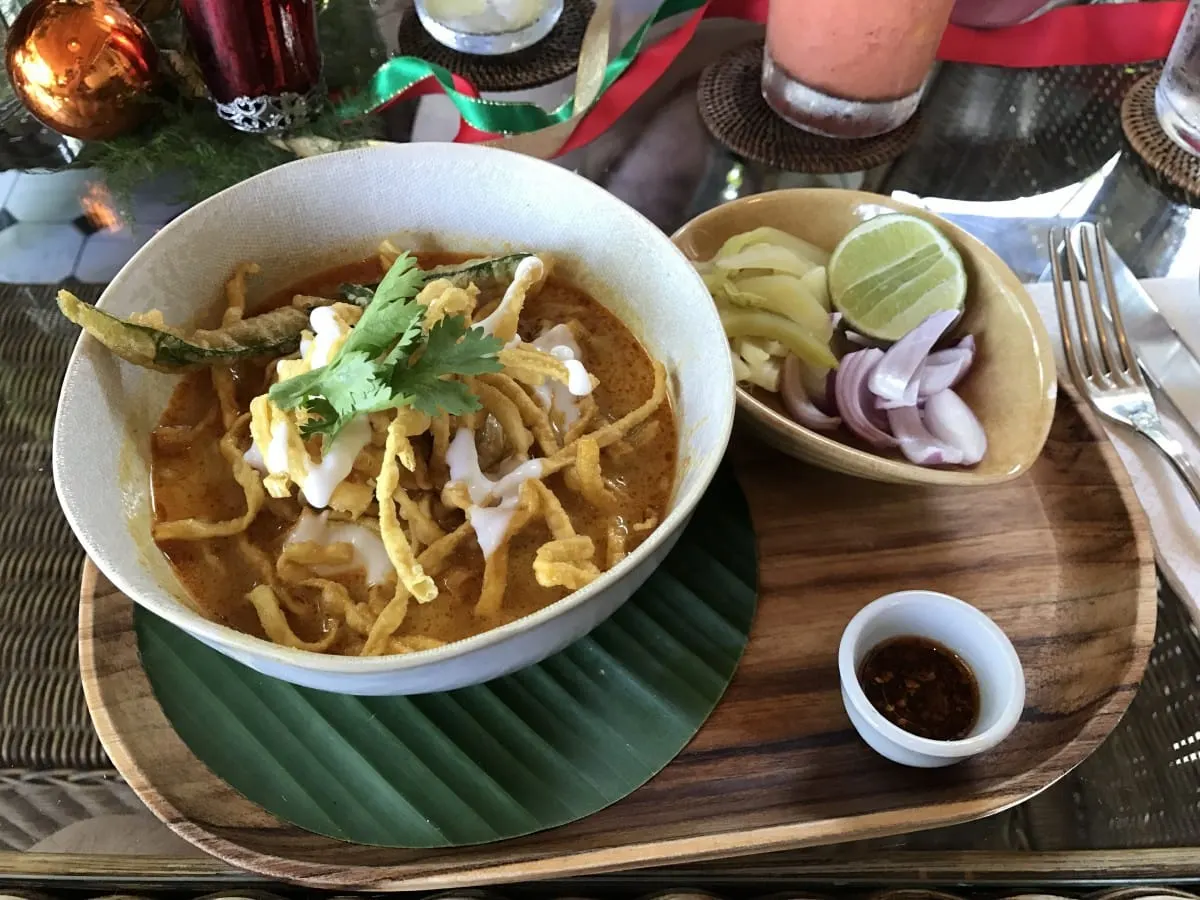Bowl of khao soi gai curry noodles with pickles, shallots and lime