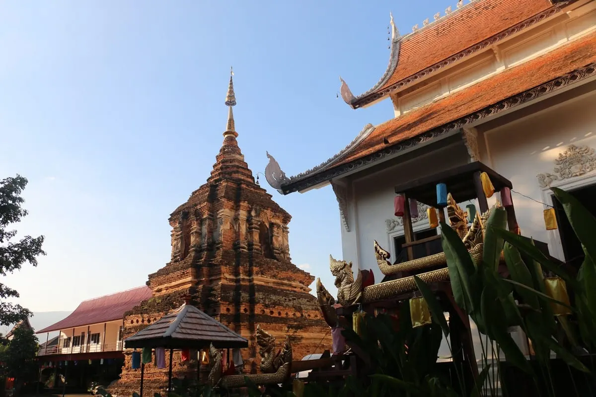Old brick chedi beside a temple hall with naga-carved roofs at Wat Chedlin