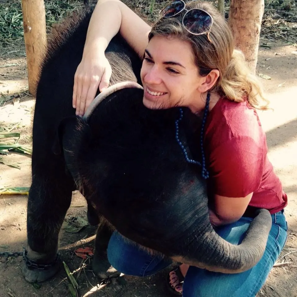 Woman in a red shirt hugging a baby elephant