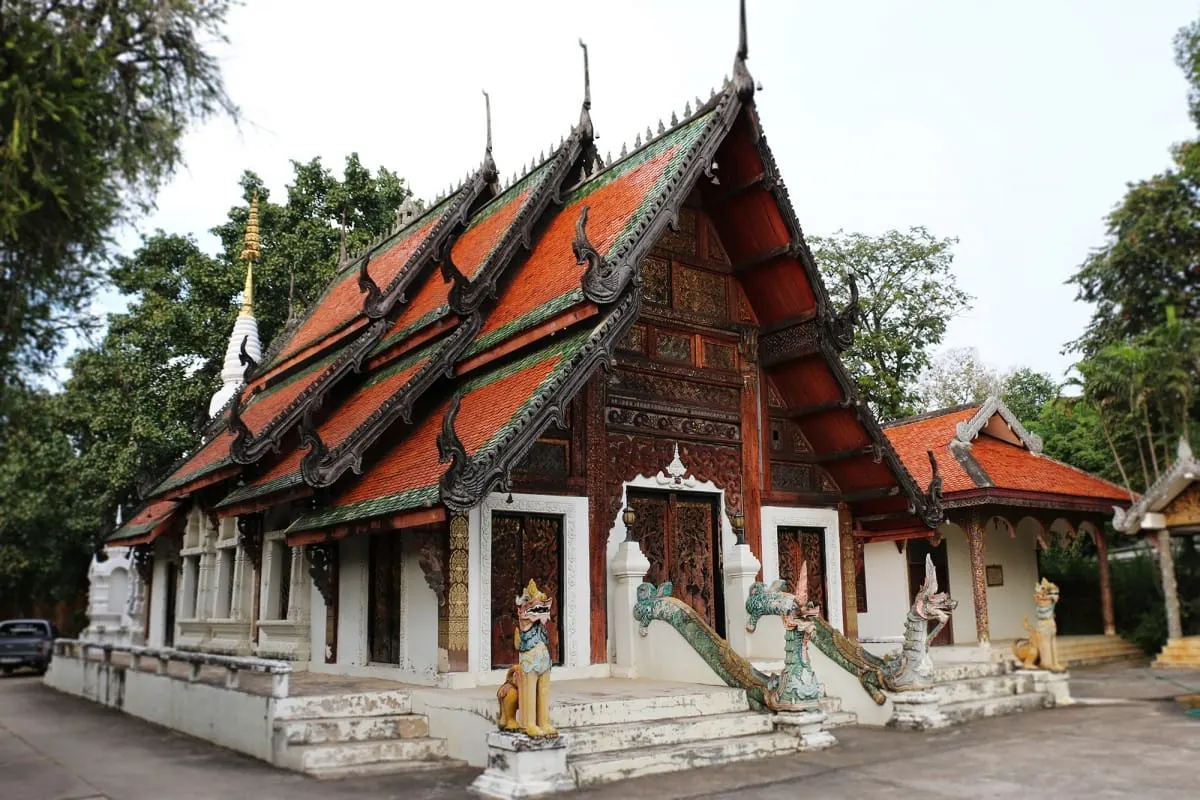 Carved teak temple with tiered orange roofs and naga stair guardians, Lampang.