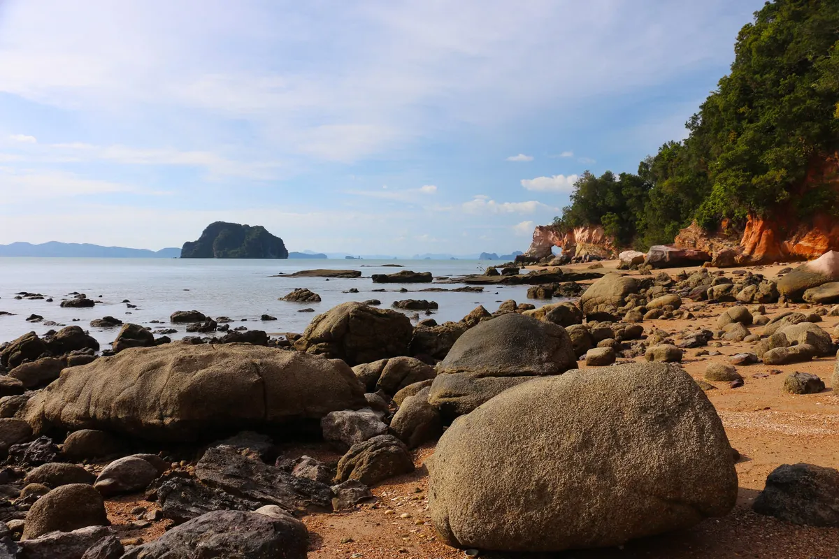 Boulders on an empty beach below orange sandstone cliffs