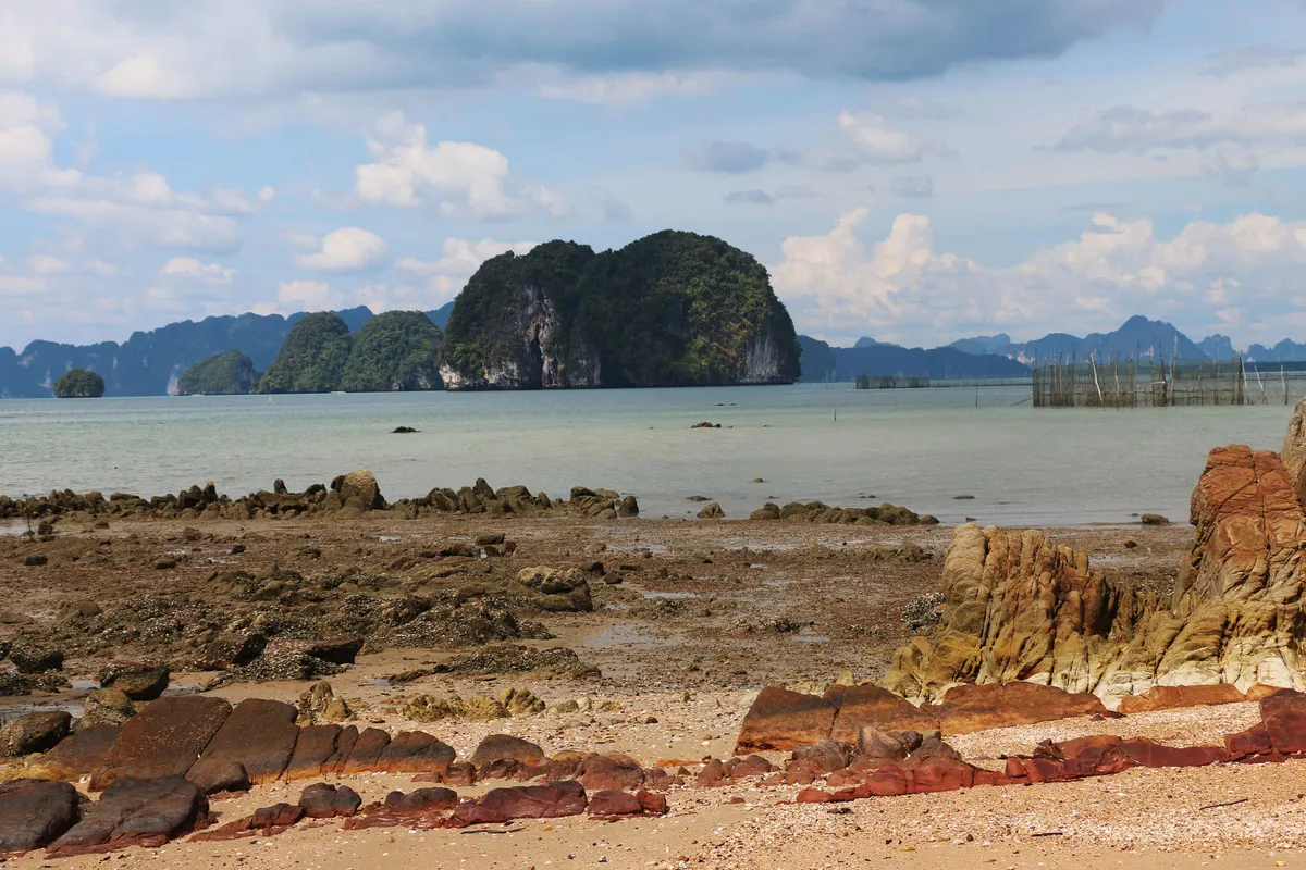 Red rocks on the shore facing a jungle-covered karst island