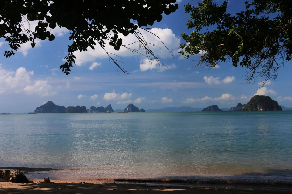 Shaded beach looking out to a calm sea and karst islands