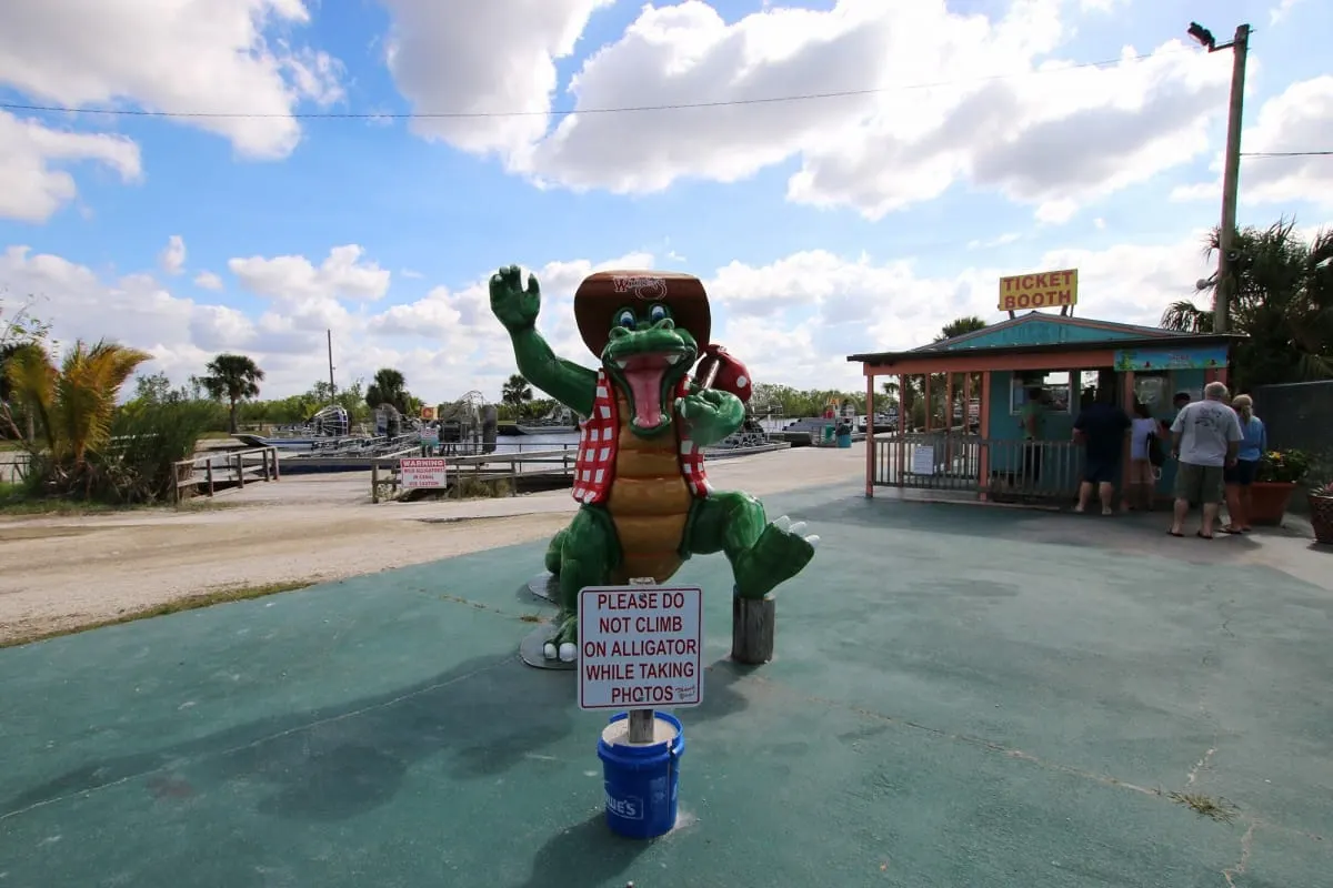 Cartoon alligator statue with a no-climbing sign by an Everglades airboat ticket booth
