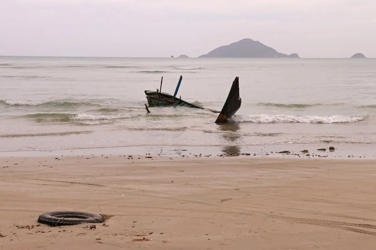 Wrecked fishing boat in the surf of a Con Dao beach, island on the horizon