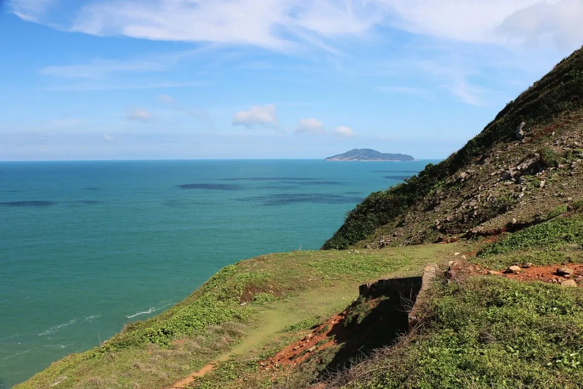 Grassy clifftop path above the green sea of Con Dao, island on the horizon