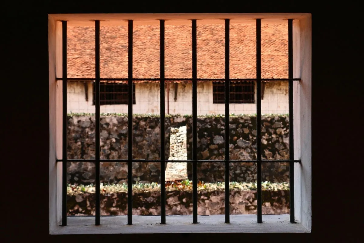 Barred window looking onto a prison courtyard wall and tiled roof, Con Dao