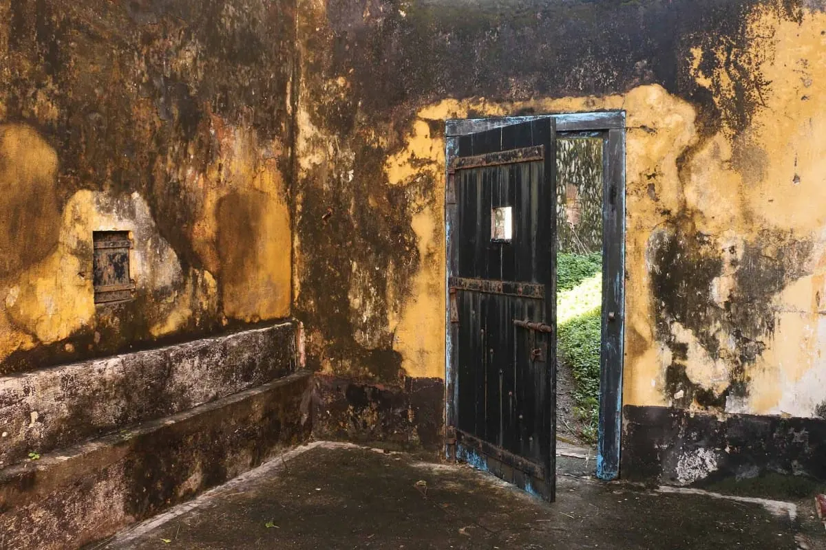 Weathered ochre prison cell with an open black door onto greenery