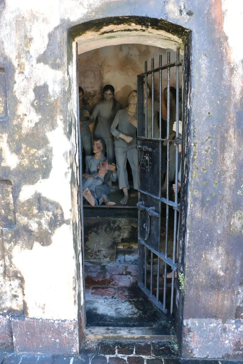 Barred door open onto a cell of prisoner statues in the Con Dao tiger cages