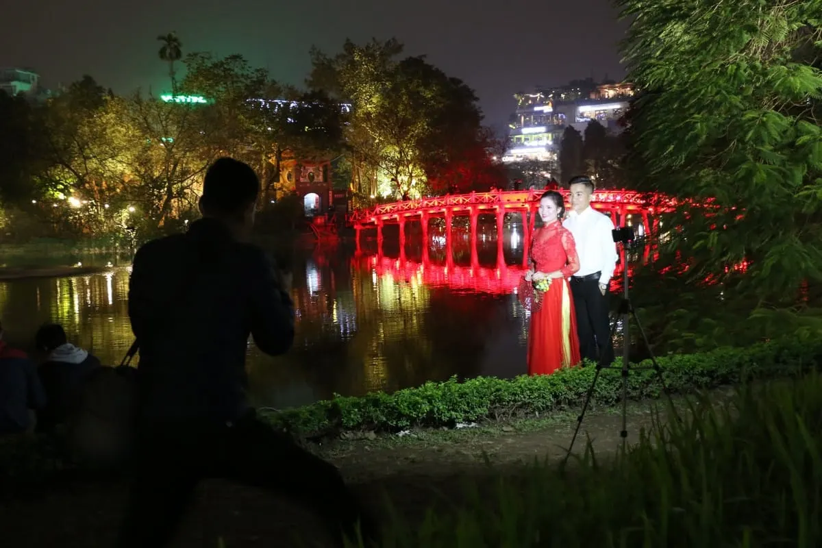Couple posing for wedding photos before Hanoi's red-lit The Huc bridge at night